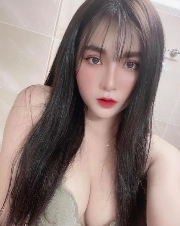 Femme aux cheveux châtains, en haut noir, regardant la caméra avec un maquillage subtil, dans un fond blanc.