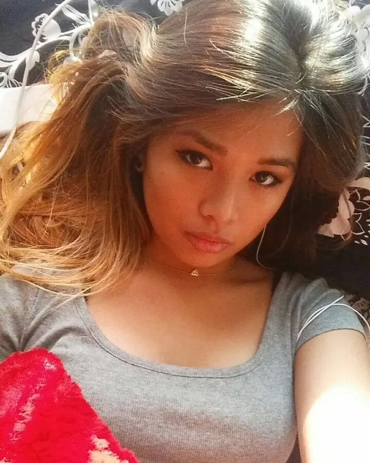 Jeune femme aux cheveux bruns, en tenue décontractée, prenant un selfie dans un cadre intérieur.