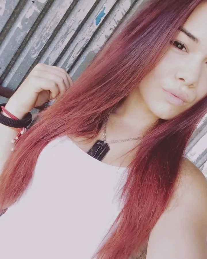 Femme aux cheveux roux, en robe blanche, posant sur un muret en pierre devant une cheminée.