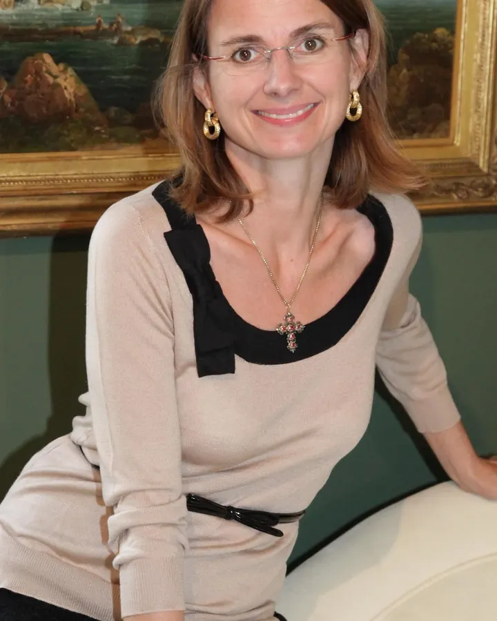 Femme aux cheveux bruns en pull beige posant devant un tableau