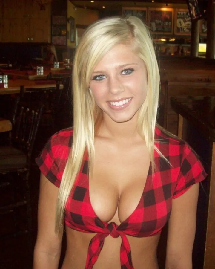 Jeune femme blonde souriante, en haut à carreaux rouge et noir, dans un bar