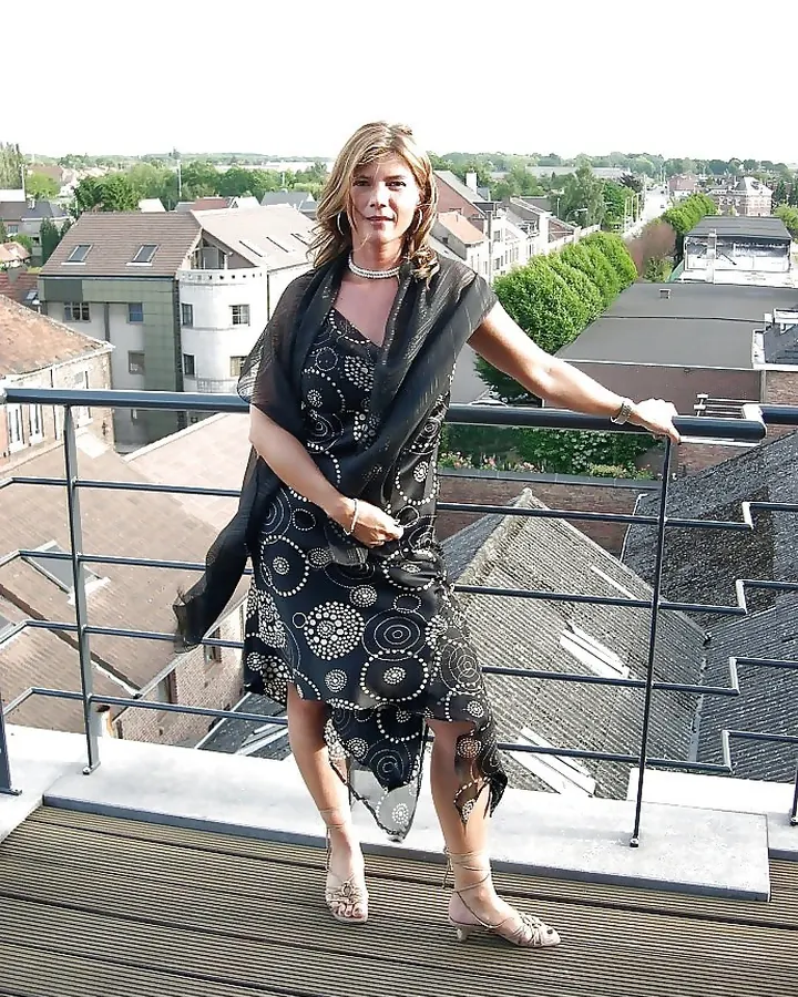 Femme en robe noire à motifs, posant sur un balcon