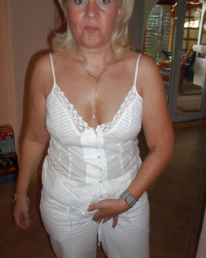 Femme blonde en haut blanc à dentelle, posant dans une pièce intérieure