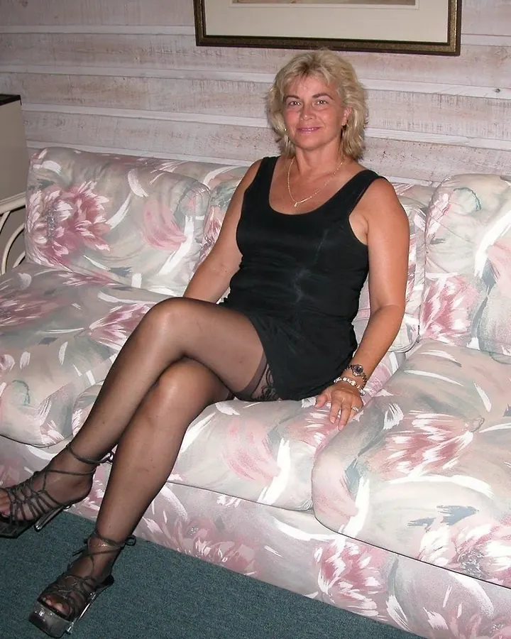 Femme en robe noire, assise sur un canapé floral, portant des sandales à talons hauts