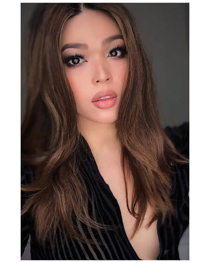 Femme aux cheveux châtains, en tenue rose, se tenant de profil près d'un mur.