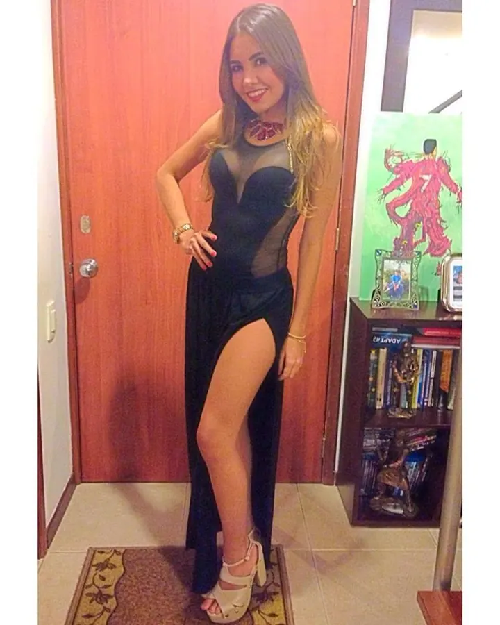 Femme en haut noir et leggings gris, prenant un selfie dans une salle de sport.