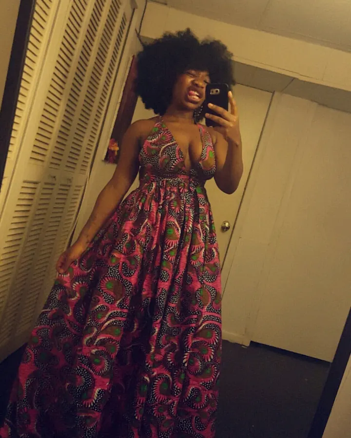 Femme aux cheveux bruns-noirs portant un haut noir et un short noir, prenant un selfie dans une salle de bain blanche.