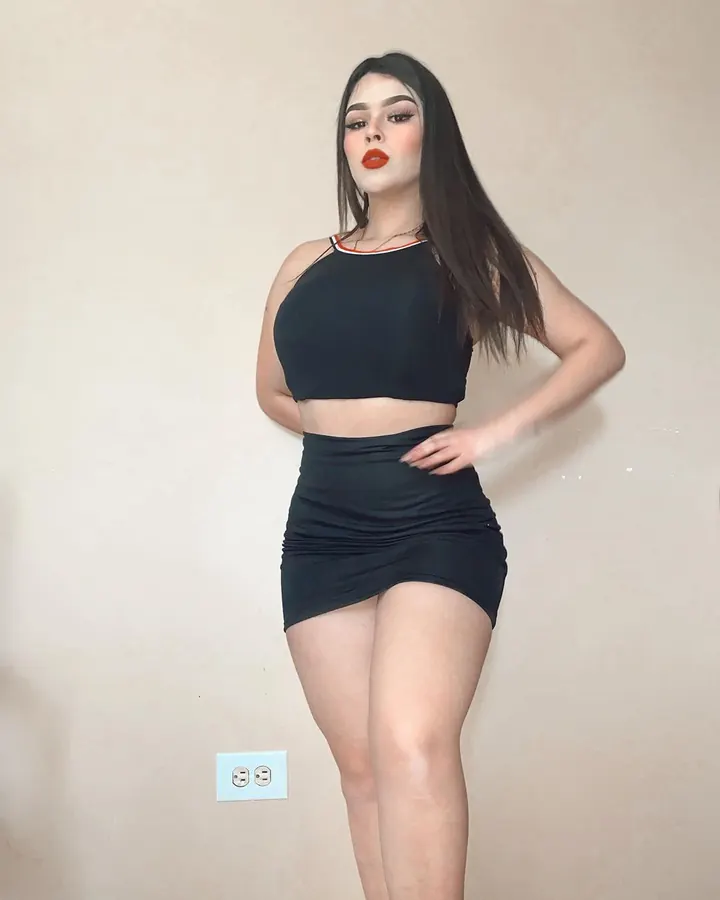 Femme en tenue noire, poitrine mise en valeur, regardant vers l'appareil.