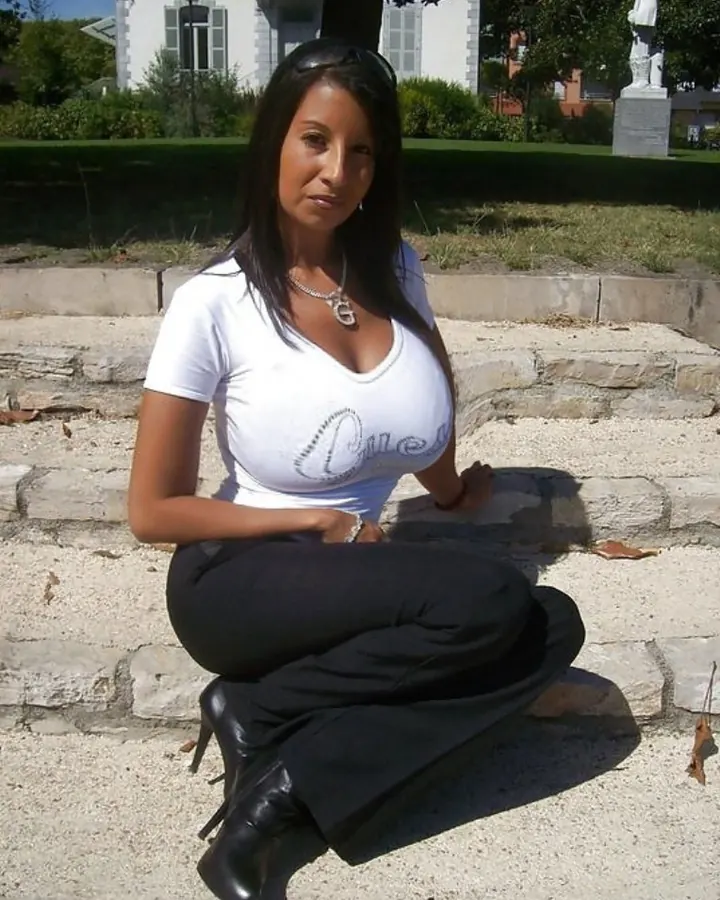 Femme aux cheveux bruns noirs en t-shirt blanc, assise sur des marches, souriant légèrement.