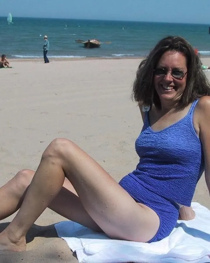 Femme en maillot bleu, assise sur le sable, plage en arrière-plan, sourire large