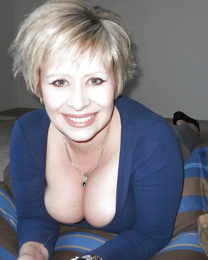 Femme aux cheveux blonds courts, souriante, en chemisier bleu, allongée sur un coussin rayé