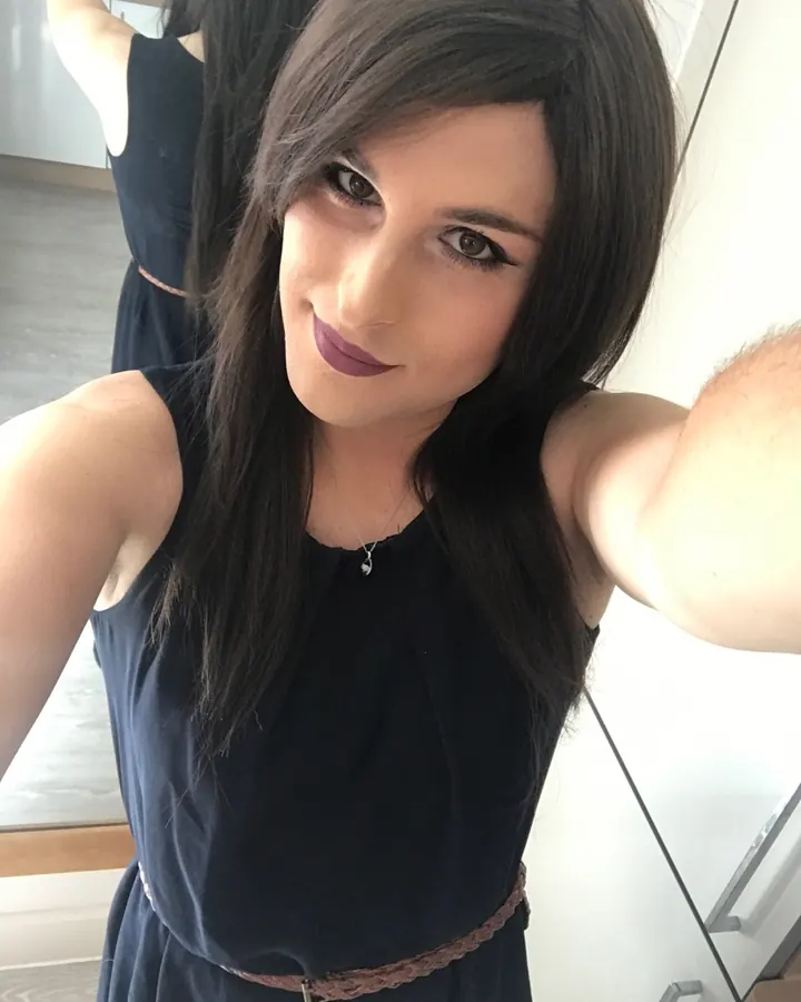 Noémie en perruque brune, robe bleue, maquillage prononcé, selfie dans cuisine