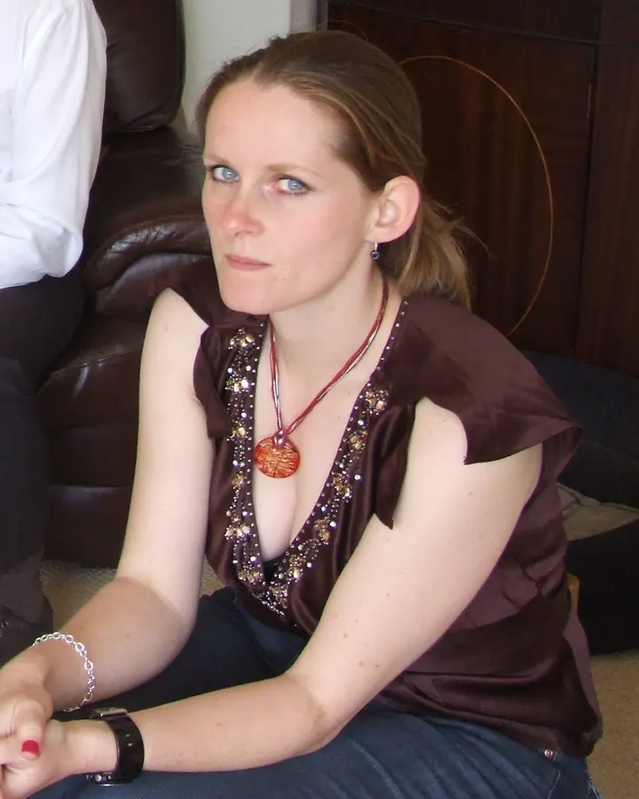 Femme aux cheveux bruns portant un haut marron orné de strass, assise sur un canapé en cuir